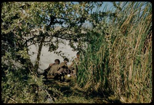 Water Hole: !U, !Ungka and another woman sitting at a waterhole, with the ledge away from Gautscha Pan in the background