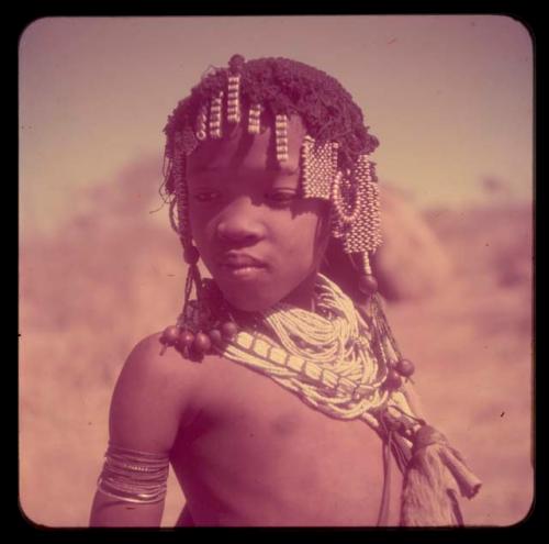 Children, Portraits: ≠Gisa wearing ornaments, including tsi, white beads around her neck and ostrich eggshell bead ornaments in her hair