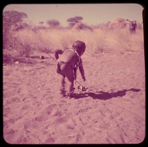 Children, Toys, Playthings: Child wearing a bag on his shoulder, pushing a toy car made from veldkos, view from behind