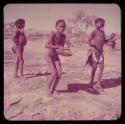 Children, Music: Boy playing the //guashi on the ledge near a waterhole, with two girls dancing next to him