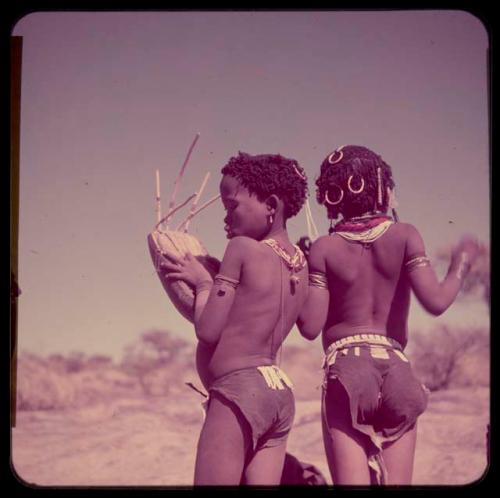 Children, Music: Two girls standing, one playing the //guashi, view from behind