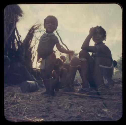 Group of women and children sitting; one child standing in the foreground