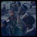 Group of women and children sitting, with a girl with ochred hair in the foreground