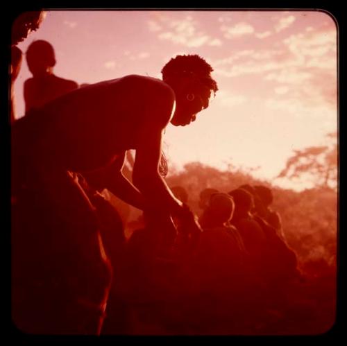 Men performing a curing dance, with a group of people sitting nearby