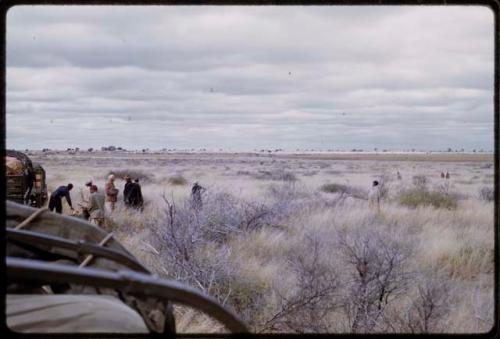 Expedition members and others standing in tall grass by expedition trucks