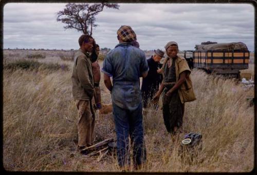 Men standing in a circle in tall grass by an expedition truck