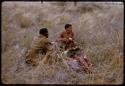 Two men sitting and eating meat, wildebeest carcass nearby