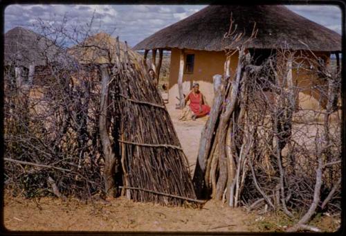 Woman sitting on porch of a house, seen through a fence