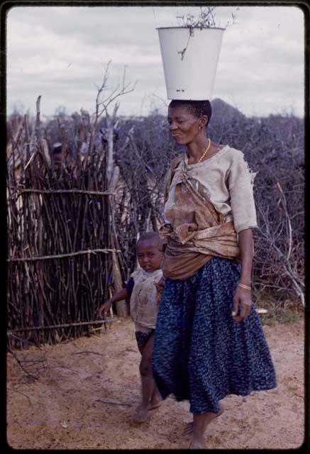 Woman carrying a bucket on her head and walking with a child