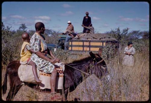 Two travelers on a donkey, Lorna Marshall and expedition members by a truck in background