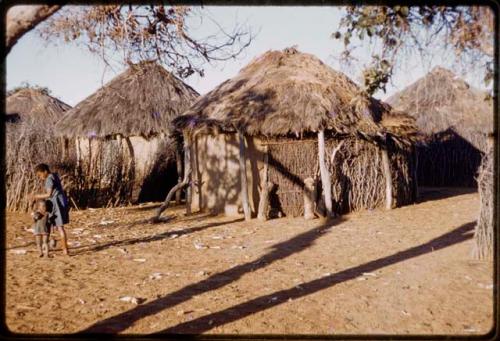 Huts, woman and child standing at the side