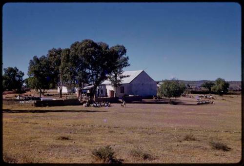 Students and teacher sitting outside, school building in background