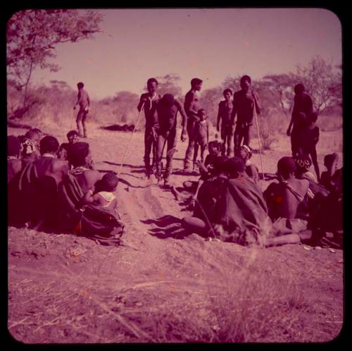 Dance: Men dancing in a line through a circle of women sitting