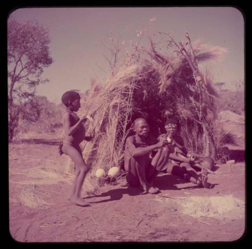 Food, Eating: //Kushay and "/Qui Navel" sitting in their skerm, eating, with one of their sons standing next to them