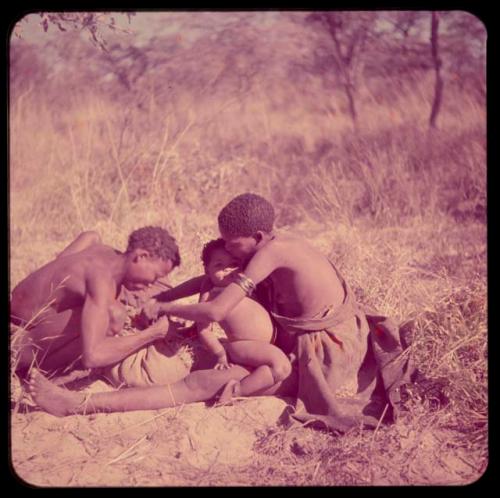 Food Gathering, "Manghettis": //Khuga holding her baby, working with "Crooked /Qui" to tie up a bundle of nuts