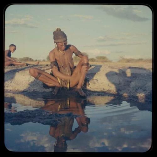 Woman sitting by pan and washing, with a child sitting in the background