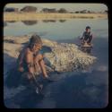 Woman sitting by pan and washing, with a boy squatting in the background