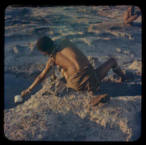 Boy scooping pan water into a cup, seen from behind