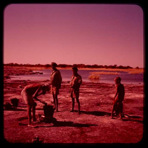 /Ti!kay tending a bucket over fire, with Tsamgao, /Gaishay and a child watching him