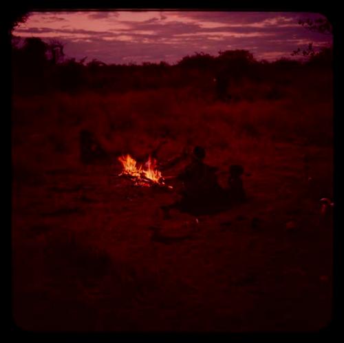 Woman and children sitting by fire, seen from behind