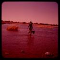 Man wading in the water, holding a bucket, seen from behind