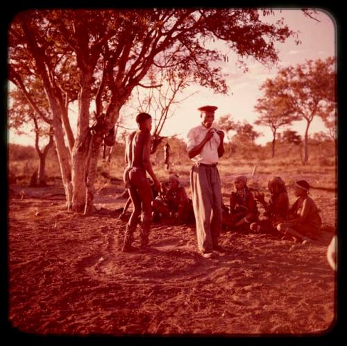 "Crooked /Qui" in Western clothes and another man dancing in a circle, with other people sitting and watching them