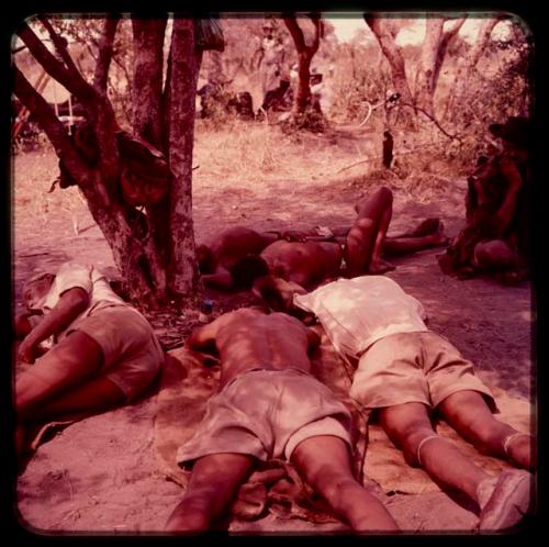 Men resting in the shade of a tree, including three men wearing Western clothes