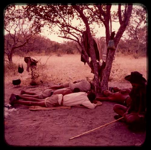 Men resting in the shade of a tree, including three men wearing Western clothes