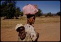 Woman with a pink bundle on her head, carrying a baby on her back