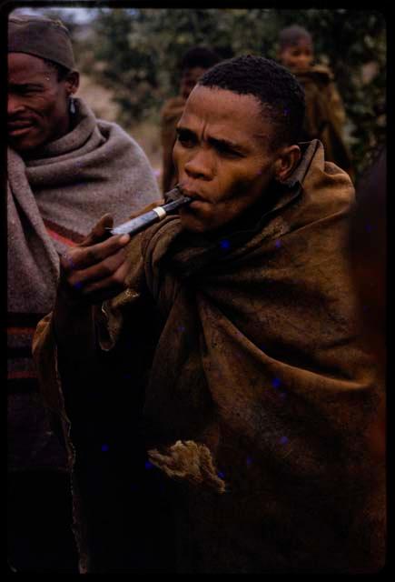 Man smoking a pipe, other people in the background