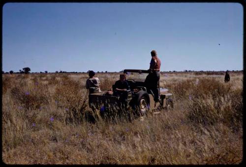 John Marshall taking a photo, Elizabeth Marshall Thomas and Theunis Berger sitting in the expedition Jeep