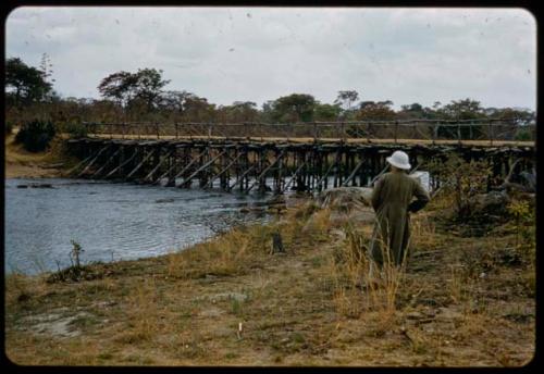 Nicolaas Jacobus van Warmelo standing on the bank of the Cubango River, looking at a bridge across it