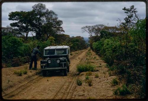 Man standing next to the expedition Land Rover on the road between Menongue and Caiundo