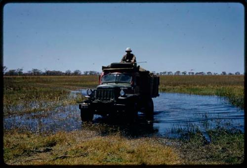 Person on top of an expedition truck driving through water in the Oshimporo omuramba