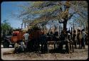 Group of people standing under a tree next to an expedition truck, having a conference with Keremendi