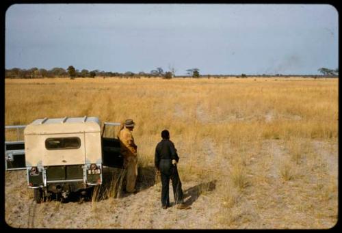 Heinrich Neumann and Philip Hameva standing next to the expedition Land Rover, with the Queen's cattle and a veld fire in the distance