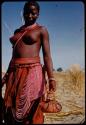 Woman wearing an ostrich eggshell bead skirt, carrying a basket decorated with beads