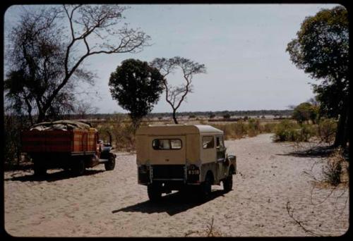 Two expedition trucks driving through heavy sand on the road at the border between South West Africa and Angola