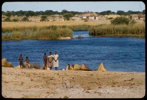 People standing next to fish traps on the shore of the Okavango River