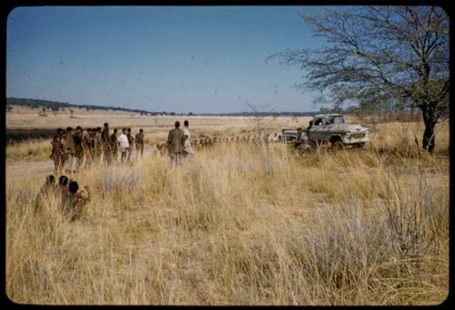 Two groups of men waiting to be paid by Mr. Kruger for work on a fire break, with Mr. Kruger sitting at a table near them