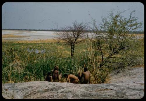 Four men sitting next to the Gautscha waterhole, with Gautscha Pan in the background