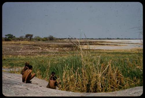 Four men sitting next to the Gautscha waterhole, with burned grass and Gautscha Pan in the background