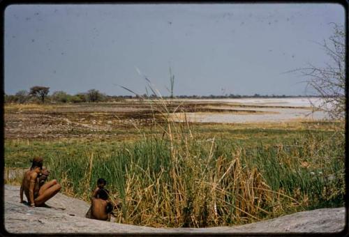 Four men sitting next to the Gautscha waterhole, with burned grass and Gautscha Pan in the background