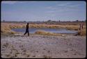 Kernel Ledimo talking by a waterhole, expedition members in the distance