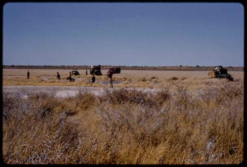 Expedition members and trucks by a waterhole, in the distance