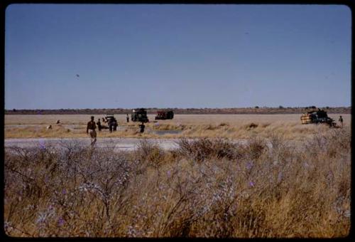 Expedition members and trucks by a waterhole, in the distance