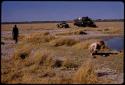 Expedition members and trucks by a waterhole, John Marshall washing his face