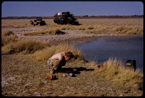 Expedition members and trucks by a waterhole, John Marshall washing his face