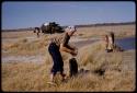 Expedition members and trucks by a waterhole, Elizabeth Marshall Thomas washing