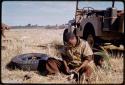 /Gishay sitting by a truck, scraping lion teeth